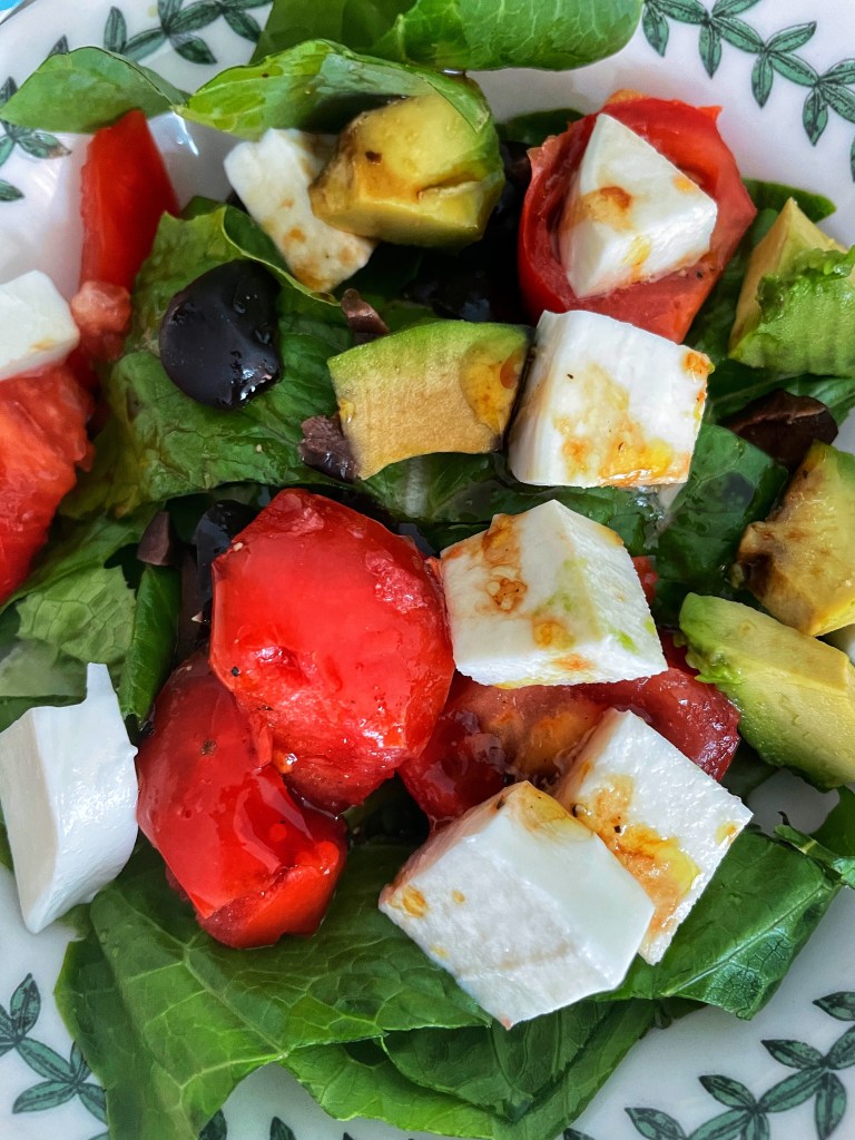Salad with greens, mozzarella tomatoes, avocado and olives, topped with olive oil and balsamic vinegar