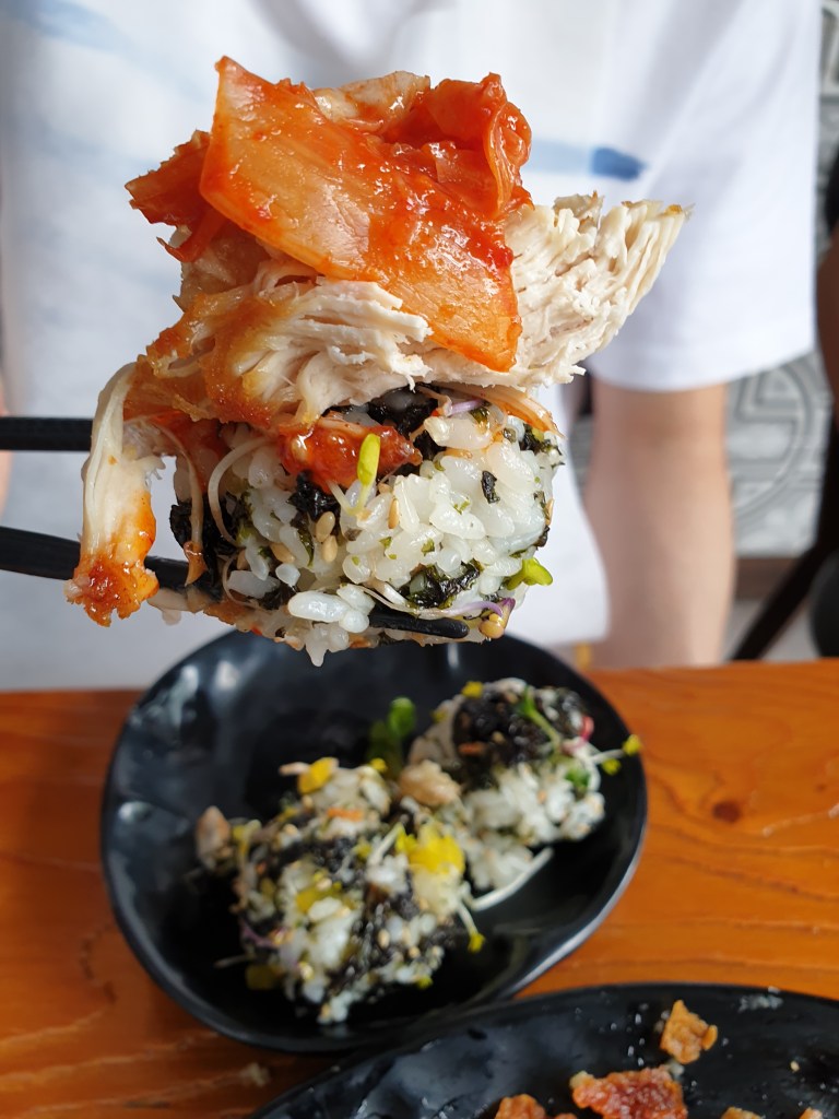 Combo of rice ball, chicken (dipped in red sauce), and kimchi on top