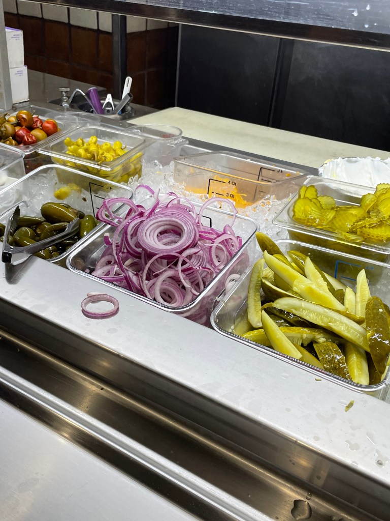 Self-serve station with red onions, pickles, and peppers